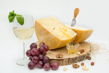 hard dressed cheese with a drop of honey, a glass of white wine and a bunch of grapes, nuts, a beautiful picture with cheese, white background, close-up