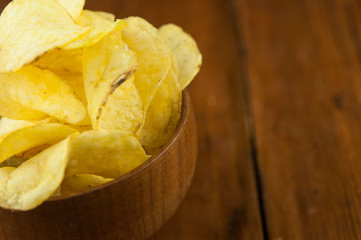 Potato chips in bowl on a wooden background, top view. Salty crisps scattered on a table.