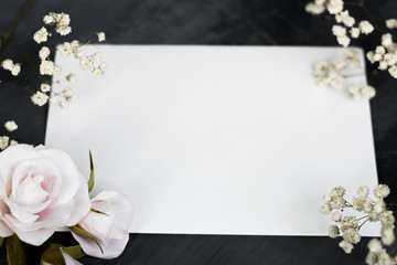 Gypsophila branches, delicate white roses and white gold wedding rings for a card or wedding invitation. White sheet of paper for inscription on a gray background, copyspace