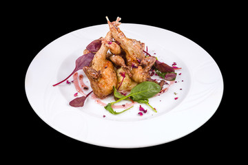 Gourmet roasted quails with sauce, arugula, and basil, on a white plate, isolated on black background
