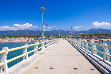 Obraz premium Forte dei Marmi, Italy - August 18, 2019: Pier, beach and Apuane mountains in Forte dei Marmi, Versilia coast, Tuscany, Italy