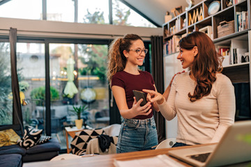 Younger roommate showing good news to her older roommate on smart phone.