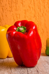 Some red, green and yellow bell peppers over a wooden surface.