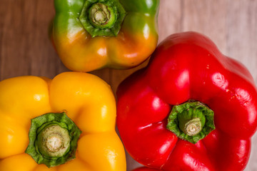 Some red, green and yellow bell peppers over a wooden surface.