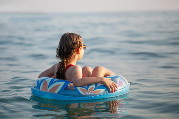 Fototapeta na wymiar young girl in glasses swims in the water on an inflatable donut in the hot sunny summer