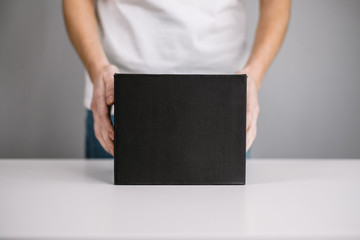 Woman holding a black cardboard box, the parcel in hands. Delivery concept, mock up.