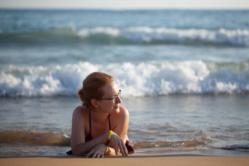 a girl with glasses lies on the beach with her back to the waves, hot sunny weather, a great time to relax