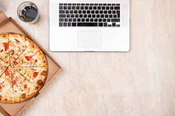 Pizza in a cardboard box and laptop on a light marble