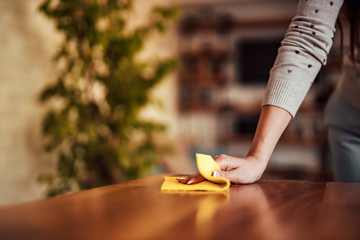 Female person wiping wooden table, close-up.