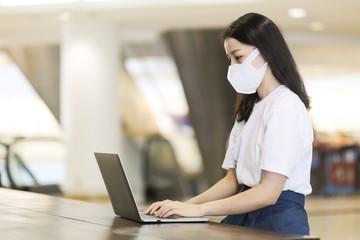 New normal lifestyle, Asian girl with laptop computer and surgical face mask to protect covid-19 in public areas