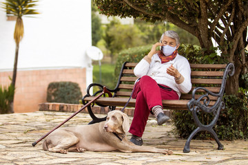 Senior woman outdoors using her cell phone wearing a home made face mask during the coronavirus quarantine de-escalation
