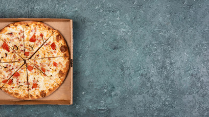 Fototapeta na wymiar Pizza in a cardboard box on a dark green textural concrete background.