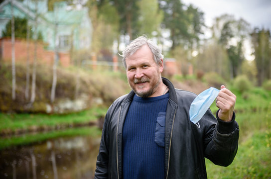 A happy middle-aged man removes a medical mask from his face in a spring Park. Over the coronavirus. End of the pandemic, epidemic, and quarantine.