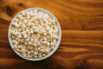 Bowl of popcorn on a wooden table, top view.