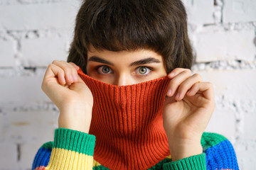 Portrait of a young woman in a multicolored sweater, covering her face with a sweater . The concept of shyness - obrazy, fototapety, plakaty