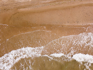 Top down view of waves breaking in the sand, flying over tropical sandy beach and waves