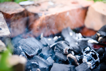 The embers of a dead fire are Smoking in the brick fence. The fire after the barbecue.