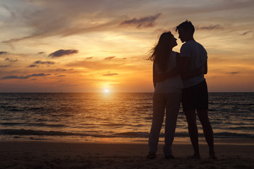 silhouette of young couple standing on beach looks at each other at orange sunset backside view copy space