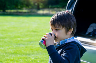 Portrait of Happy boy standing next ot a car drinking soda with a happy face, Active child boy traveling by car with parent during school break in summer, Kid drinking drinking soft drink.