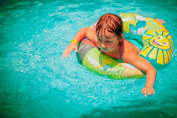 Portrait of beautiful child girl in swimming pool relax swim on inflatable ring. Summer holiday, vacation and happy childhood. Horizontal image.