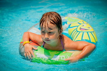 Close up portrait of beautiful child girl in swimming pool relax swim on inflatable ring. Summer holiday, vacation and happy childhood. Horizontal image.
