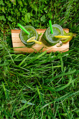 Green homemade cocktails in two glass jars stand in the thick green grass in the garden. Ingredients-lemon, spinach, kiwi, Basil. The concept of healthy eating, detox