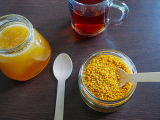beekeeping products-honey and pollen pellets in a glass container and a Cup of tea on a dark table surface