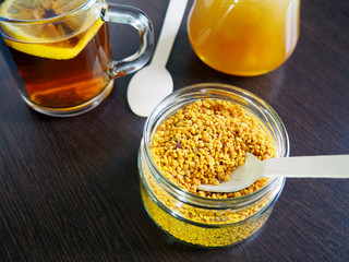 bee products-honey and pollen in a glass container and a Cup of tea with lemon on the dark surface of the table