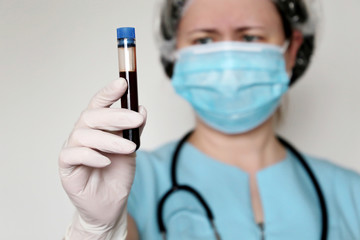 Test tube in female hand close up, woman in medical mask holding a vial with red liquid. Concept of...