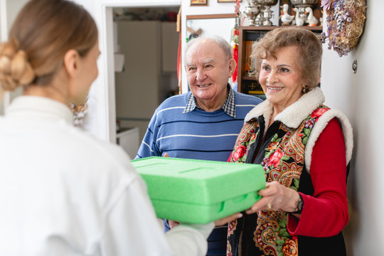Senior couple greeting volunteer delivering a hot meal to their door