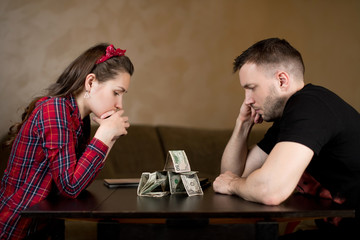 Married couple sadly looks at a house, folded on a table from cash savings