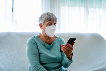 Caucasian senior woman sitting with face mask looking at mobile phone