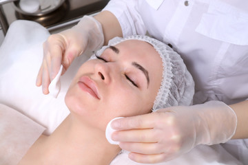 Naklejka premium Beautician makes the cleansing procedure a young beautiful girl patient. The concept of skin care face and body