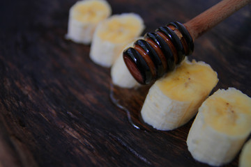 
honey dipper on, background of a banana with liquid honey, in a wooden plate.