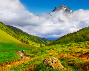 Naklejka premium beautiful green mountain valley and high mount peak in a dense clouds