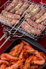 raw sausages and langoustines into grill grate on the red table are ready to be grilled