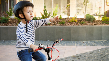 Portrait of excited little boy riding bicycle and pointing with finger