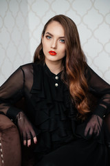 Portrait of beautiful elegant woman in black dress sitting on armchair.