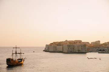 The old city of Dubrovnik against the sunset sky. The wooden sailing ship Galleon approaches the main pier of Dubrovnik.