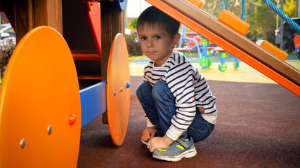 Portrait of sad crying boy sitting under slide on children playground at park
