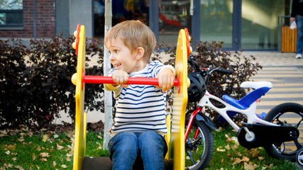 Portrait of happy laughing little boy riding on children playground at park