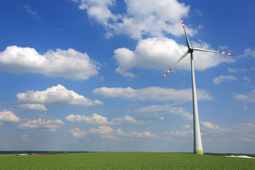 Turbina wiatrowa, wiatrak na zielonym polu, na tle niebieskiego nieba z chmurami.