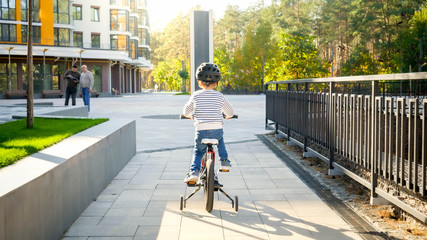 Little boy riding his bicycl on city street at sunny day