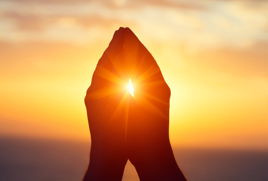 silhouette of male  raising hands praying for God's blessings at sunset or sunrise light, practicing yoga on the beach, religion, freedom and spirituality concept