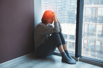 young stressed tired woman sitting on the floor at home suffering from migraine headache, having...