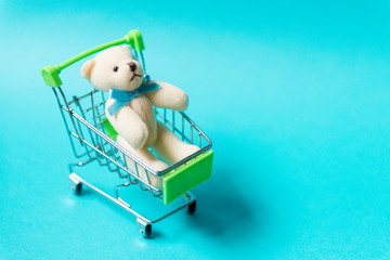 Shopping cart with teddy bear on blue background. Children's day concept.