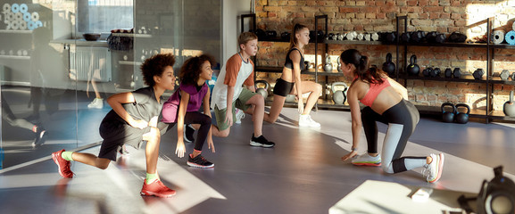 Health care for life. Portrait of teens, boys and girls warming up, exercising with female trainer in gym. Sport, healthy lifestyle, physical education concept