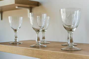 Many transparent crystal glasses stand in a row on a wooden shelf. Side view. Tasting concept, interior