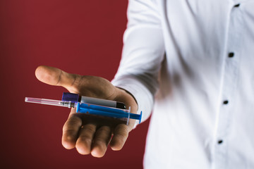 man holding a syringe and ampoule with blood in his hand on his palm isolated on red background. Danger. Pandimia.