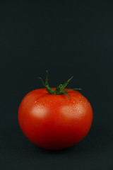 bright red tomato with water droplets on a black background in the center of the photograph
